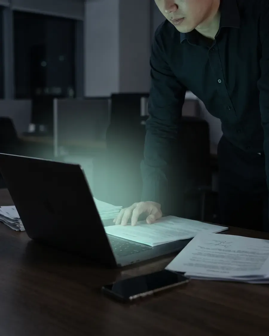 Signed agreements on a dark desk beside a laptop showing an approval queue.