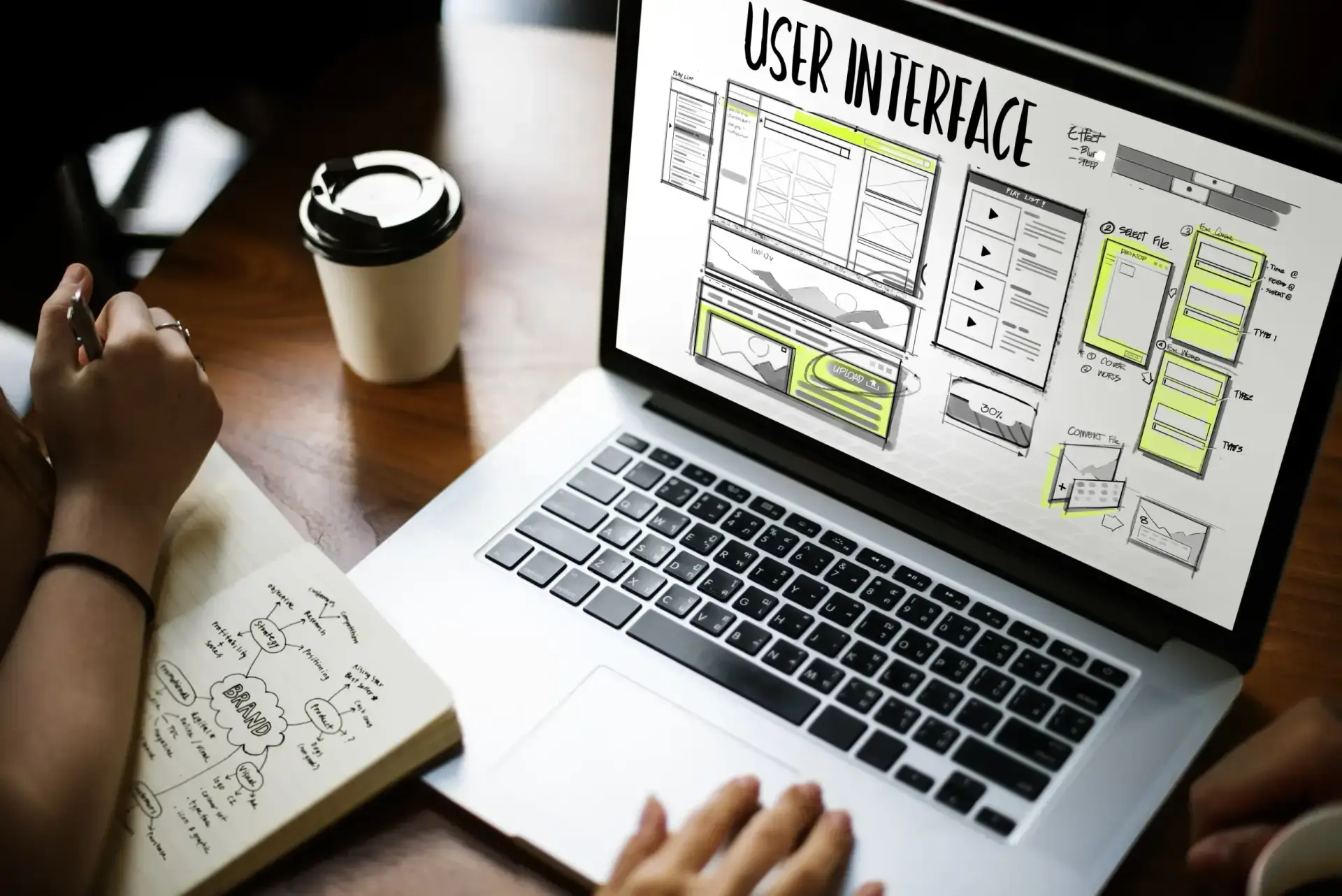A designer sketching interface layouts beside a large monitor.